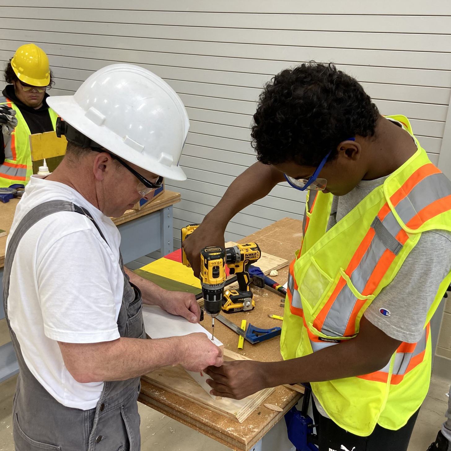 An instructor helps a student learning carpenter skills.