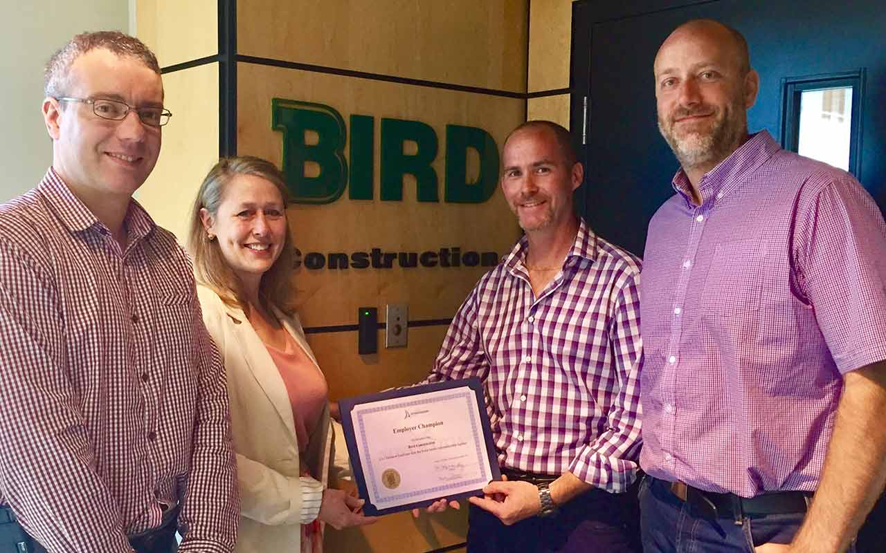 Employees of Bird Construction gather around their Employer Champion award
