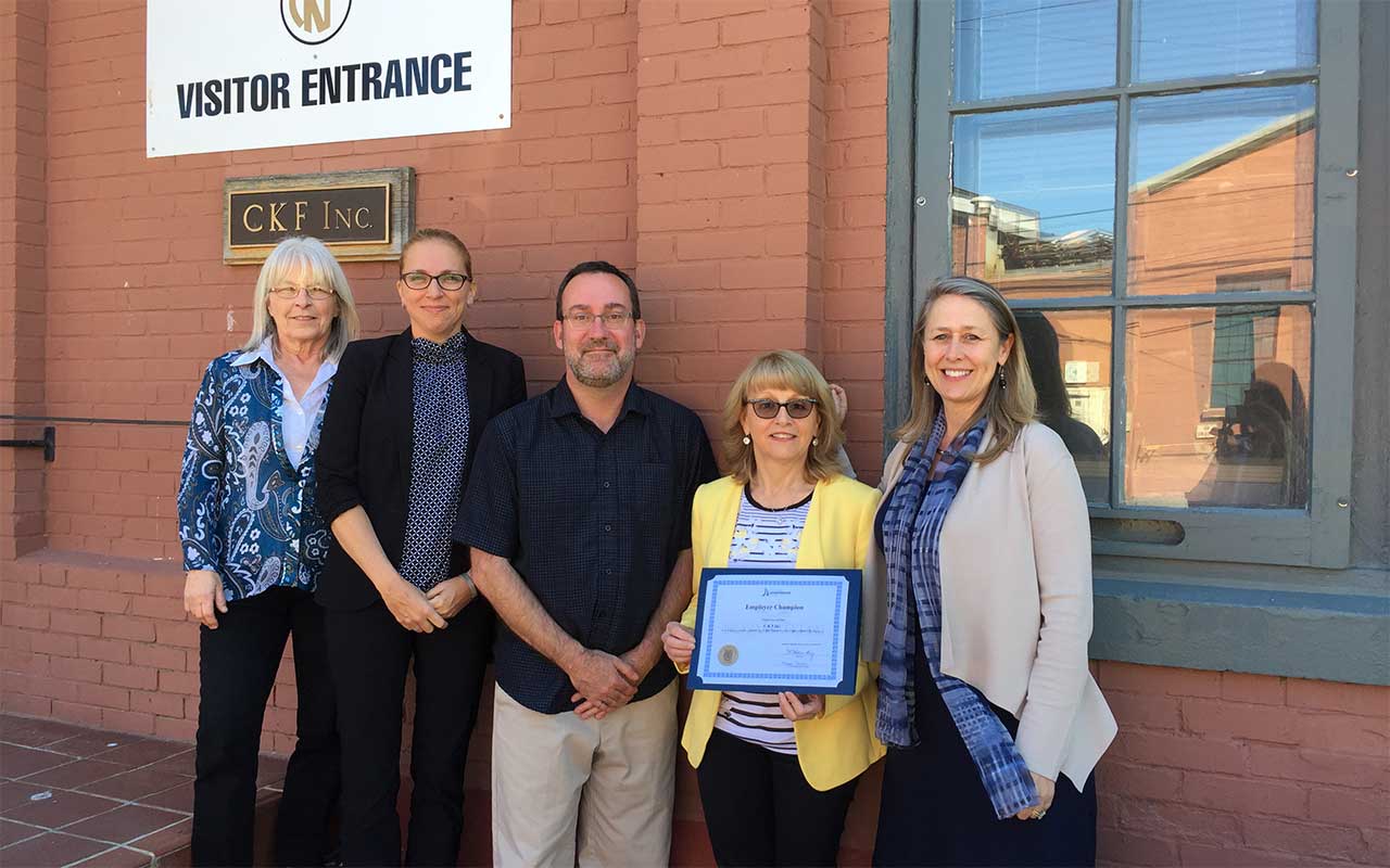 Employees of CKF Inc. gather around their Employer Champion award