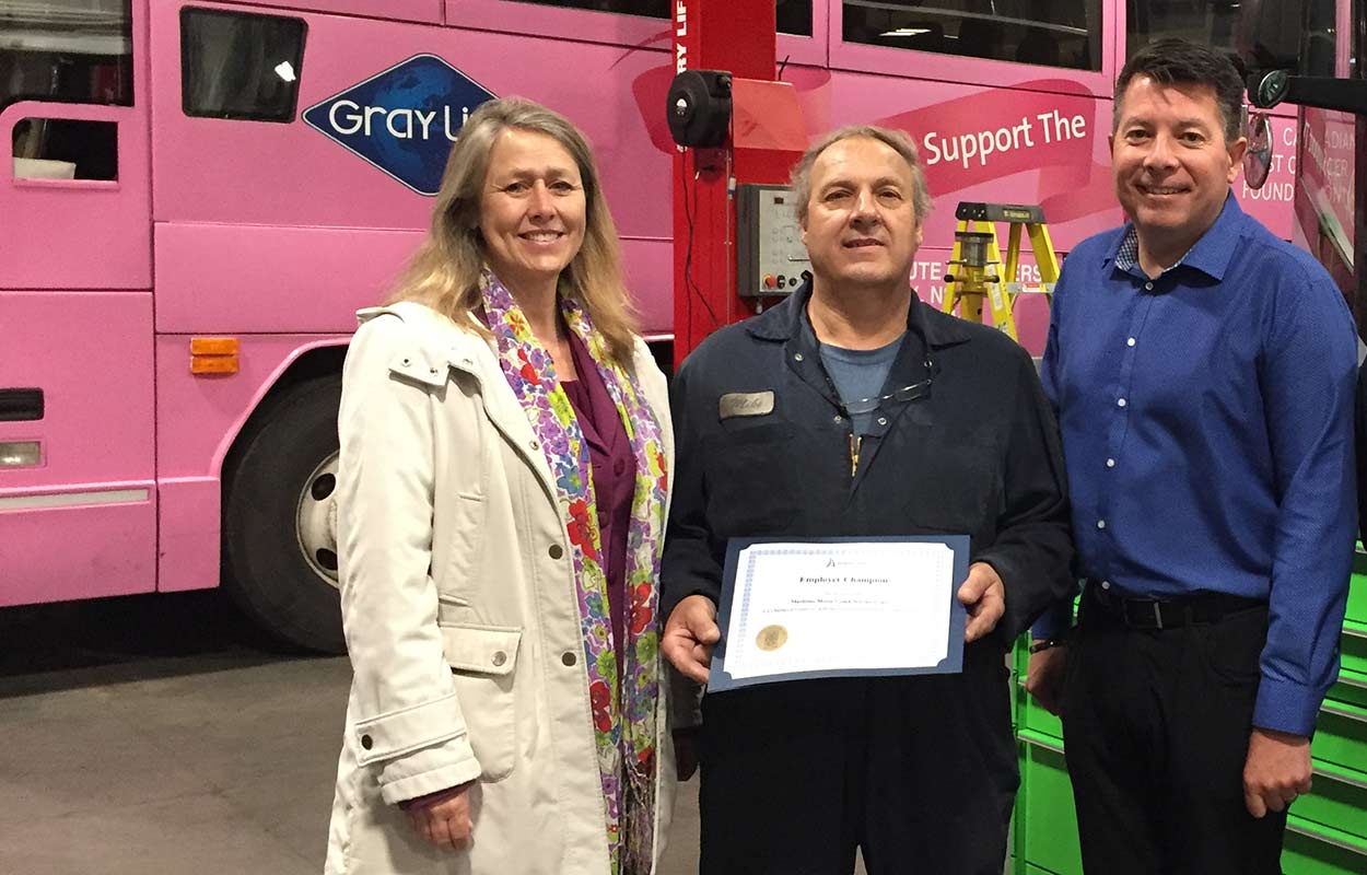 Employees of Maritime Motor Coach gather around their Employer Champion award