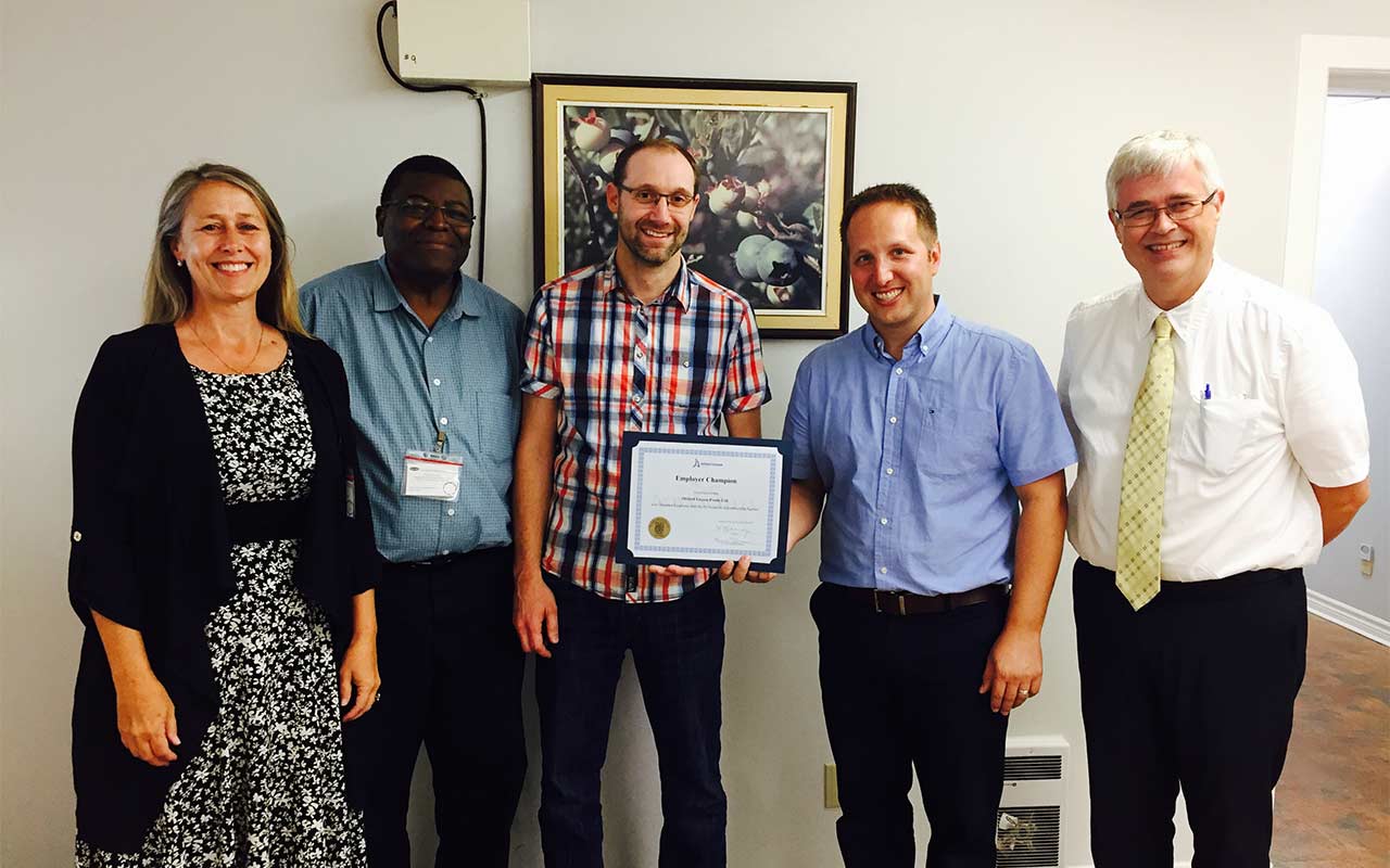 Employees of Oxford Frozen Foods gather around their Employer Champion award