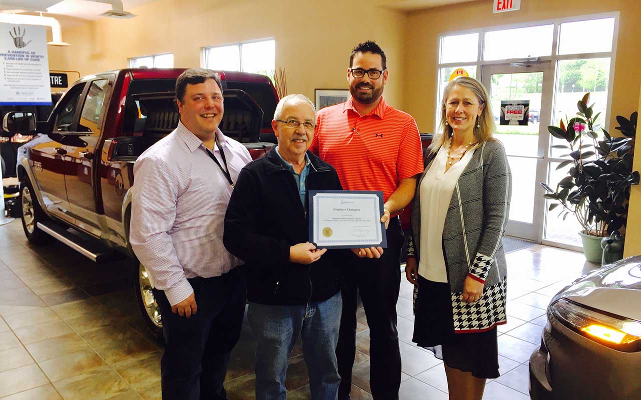 Employees of Saunders Motors Company gather around their Employer Champion award