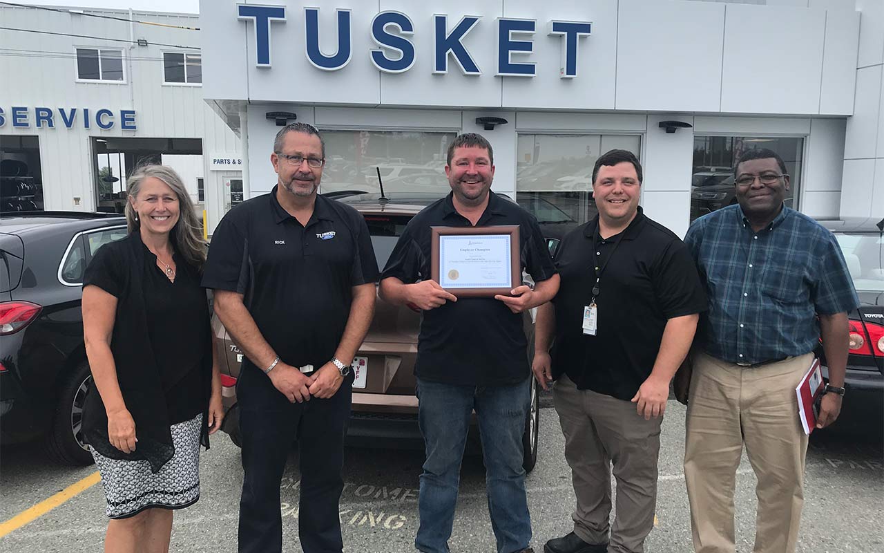 Employees of Tusket Sales and Service gather around their Employer Champion award