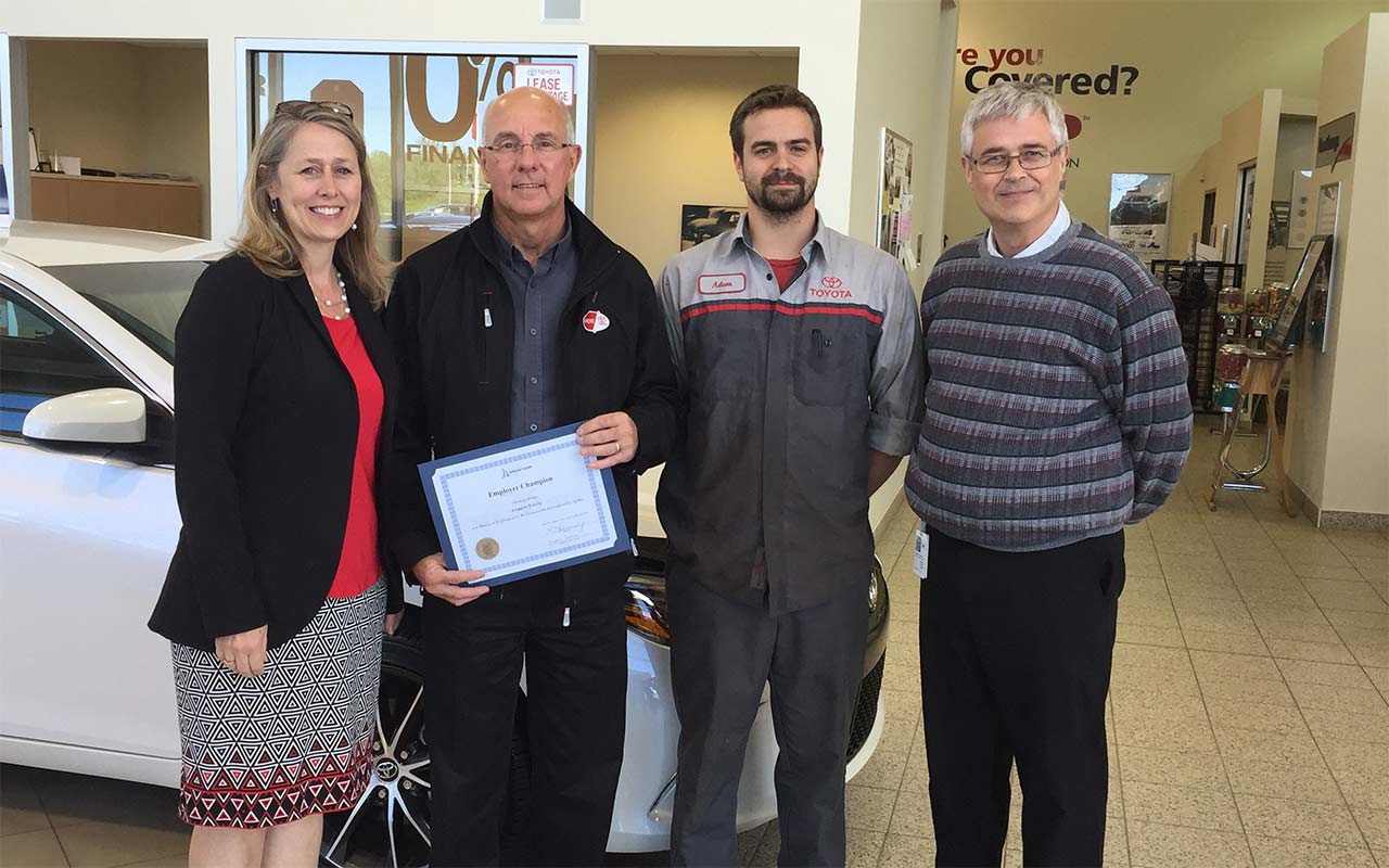 Employees of Amherst Toyota gather around their Employer Champion award