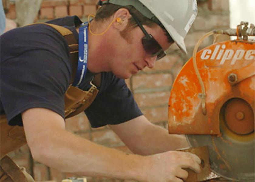 A young man uses a buffer machine on a brick while wearing a hard hat and safety goggles